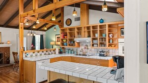 Una cocina con vigas de madera, encimera de baldosas blancas y estantería empotrada.
