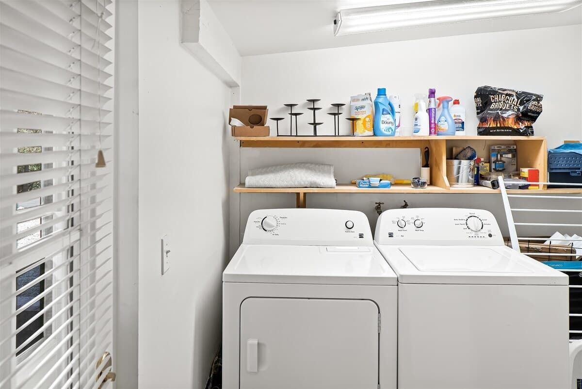 A laundry room with two white front-loading washers, shelves with cleaning supplies, and a towel rack.