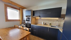 Eine kleine Küche mit dunklen Schränken, einem Holztisch und einem eingebauten Backofen.