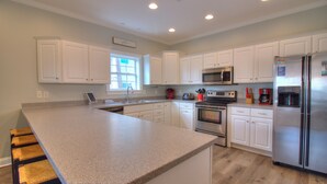 Una cocina moderna con armarios blancos, encimera de granito, electrodomésticos de acero inoxidable y un ventanal que proporciona luz natural.