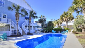 Una piscina con cubierta blanca, rodeada de palmeras y un edificio de dos pisos con balcones.