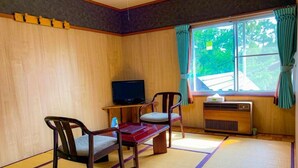 Une pièce de style japonais traditionnel, avec un sol recouvert de tatamis, une télévision, un radiateur et une fenêtre avec des rideaux.