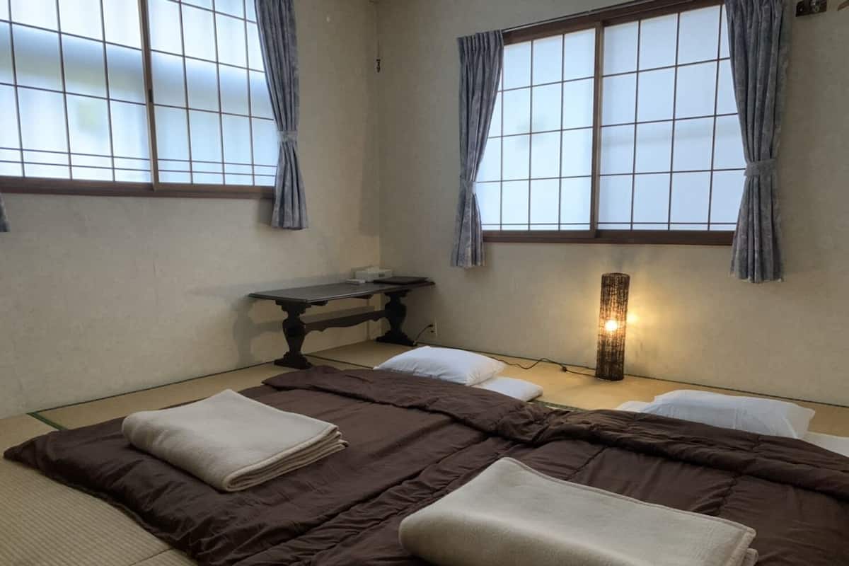 Ein traditioneller japanischer Raum mit Tatami-Böden, einem niedrigen Tisch und einem Bett mit dunkelbrauner Bettdecke und weißen Kissen.
