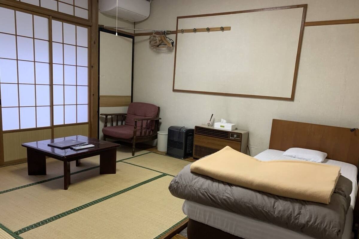 Ein traditioneller japanischer Raum mit Tatami-Boden, einem Futon, einem Holzstuhl, einem kleinen Tisch und einem Radio.