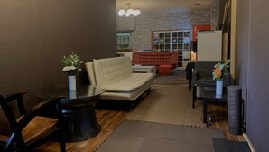 Un salon moderne avec un canapé, des fauteuils et une table basse. On y trouve un mur en pierre et une porte qui donne sur une autre pièce.