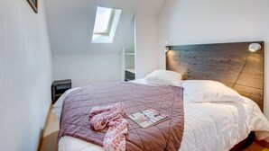 Quarto com teto inclinado, claraboia, cabeceira de madeira e cama com colcha acolchoada.