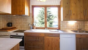 A kitchen with wooden cabinets, a stove, a dishwasher, and a window with a view of trees.