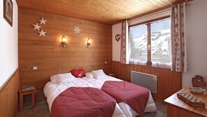 A cozy wooden cabin room with a bed, two bedside tables, a window with curtains, and a view of a snowy landscape.