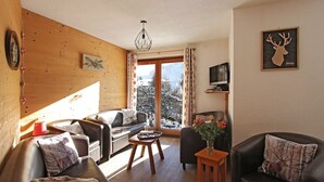 A cozy living room with a wooden wall, a sofa, a coffee table, and a television on a stand.