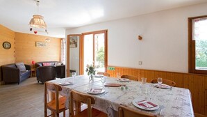 A dining area with a table set for four, wooden walls, and a view through an open door.