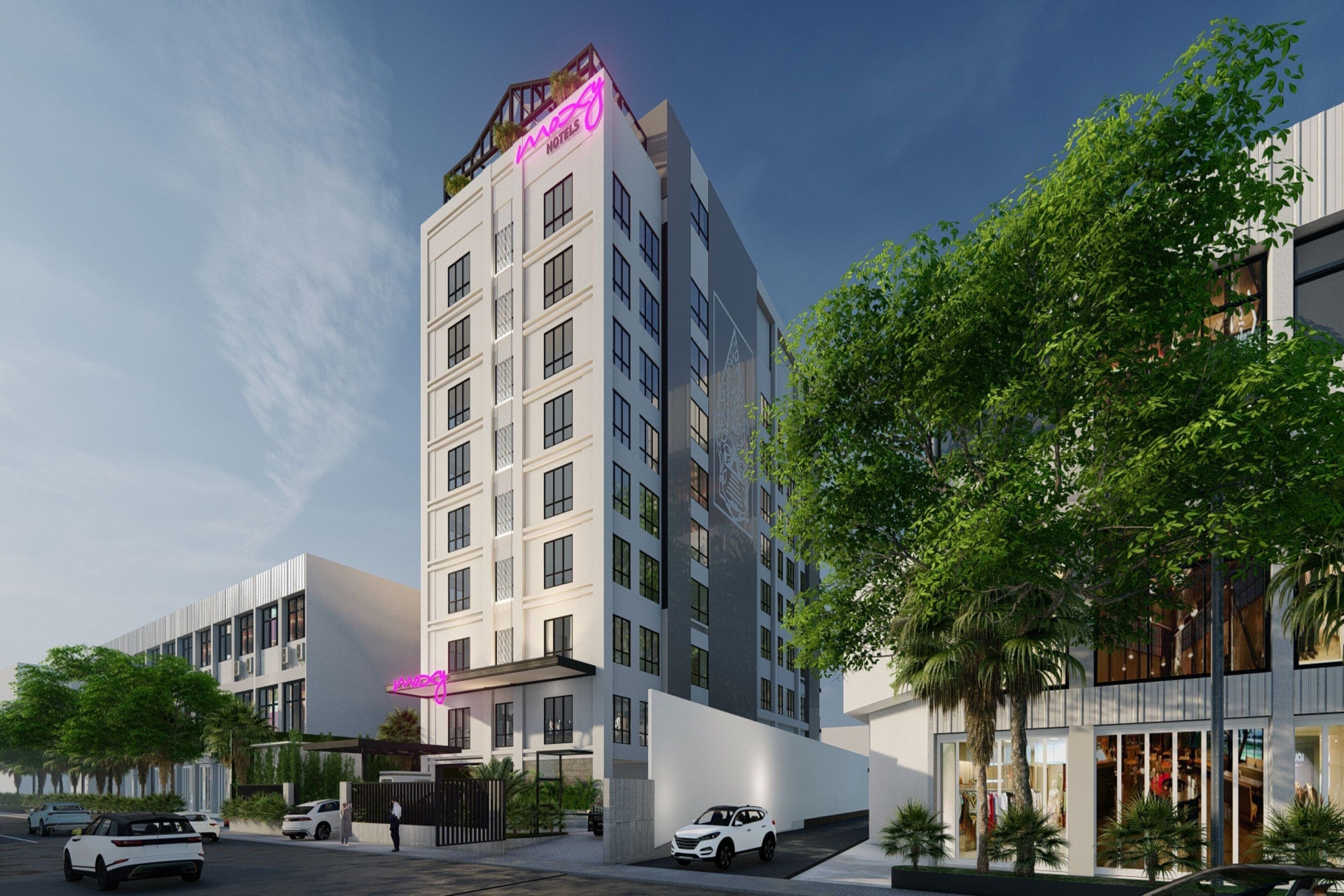 A modern hotel with a prominent neon sign, multiple floors, and a parking area with cars.
