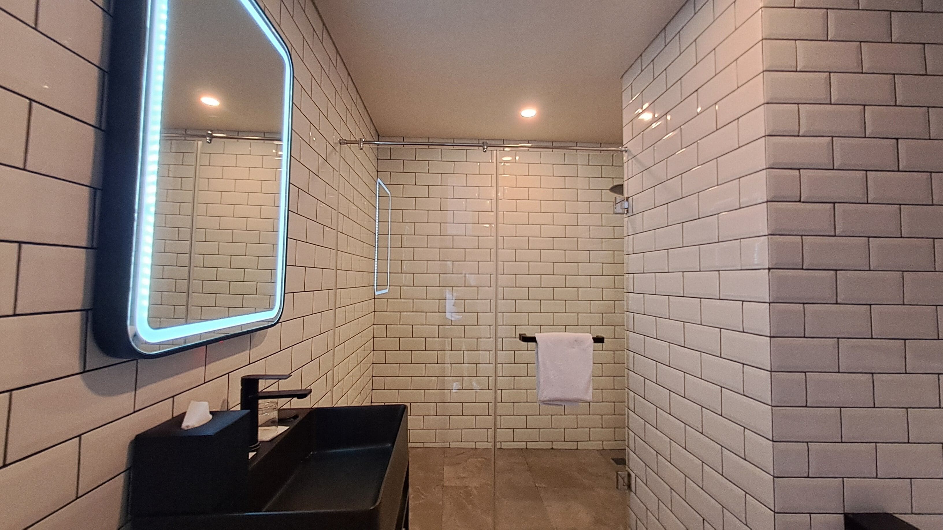 Un baño moderno con un lavamanos negro, un espejo con luces LED y una zona de ducha.