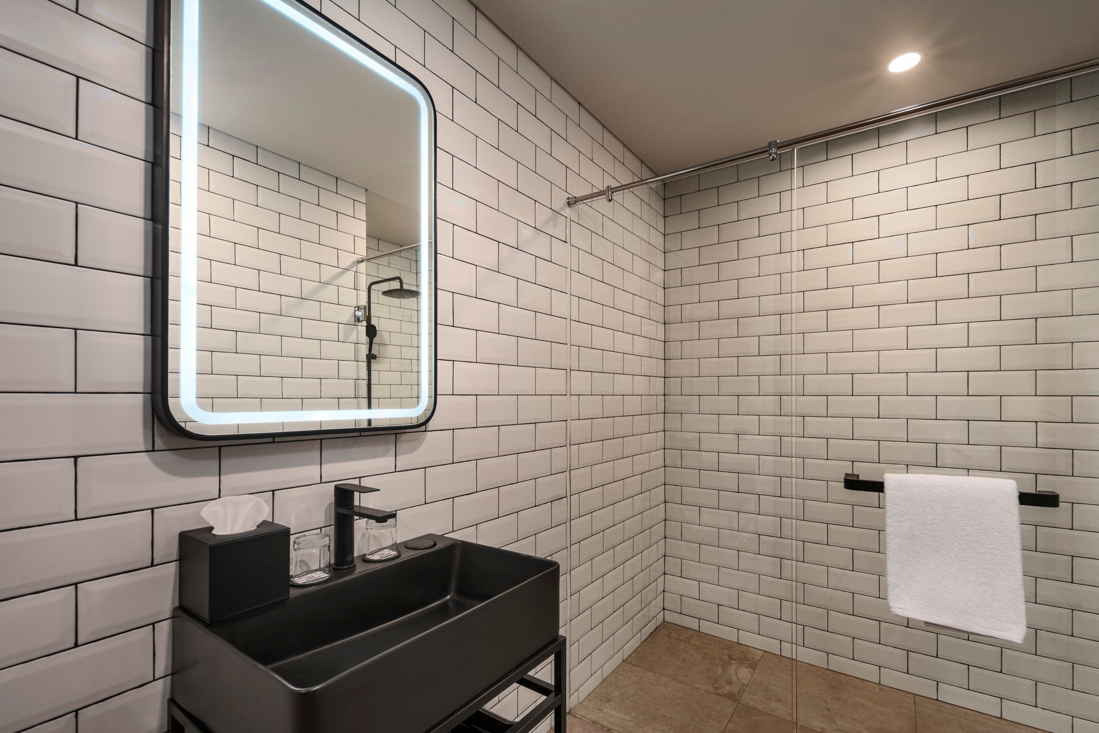 A modern bathroom with white subway tiles, a black sink, a mirror with LED lighting, and a towel rack.