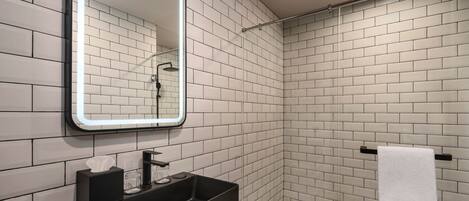 A modern bathroom with white subway tiles, a black sink, a mirror with LED lighting, and a towel rack.