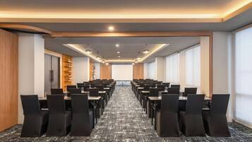 A conference room with rows of tables and chairs, a projector screen, and a wooden panel wall.