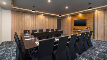 Une salle de conférence avec une longue table, des chaises, un téléviseur à écran plat et des murs recouverts de panneaux en bois.