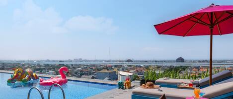 Una piscina en la azotea con sillones de descanso, un flotador con forma de flamenco rosa y vistas a la ciudad.