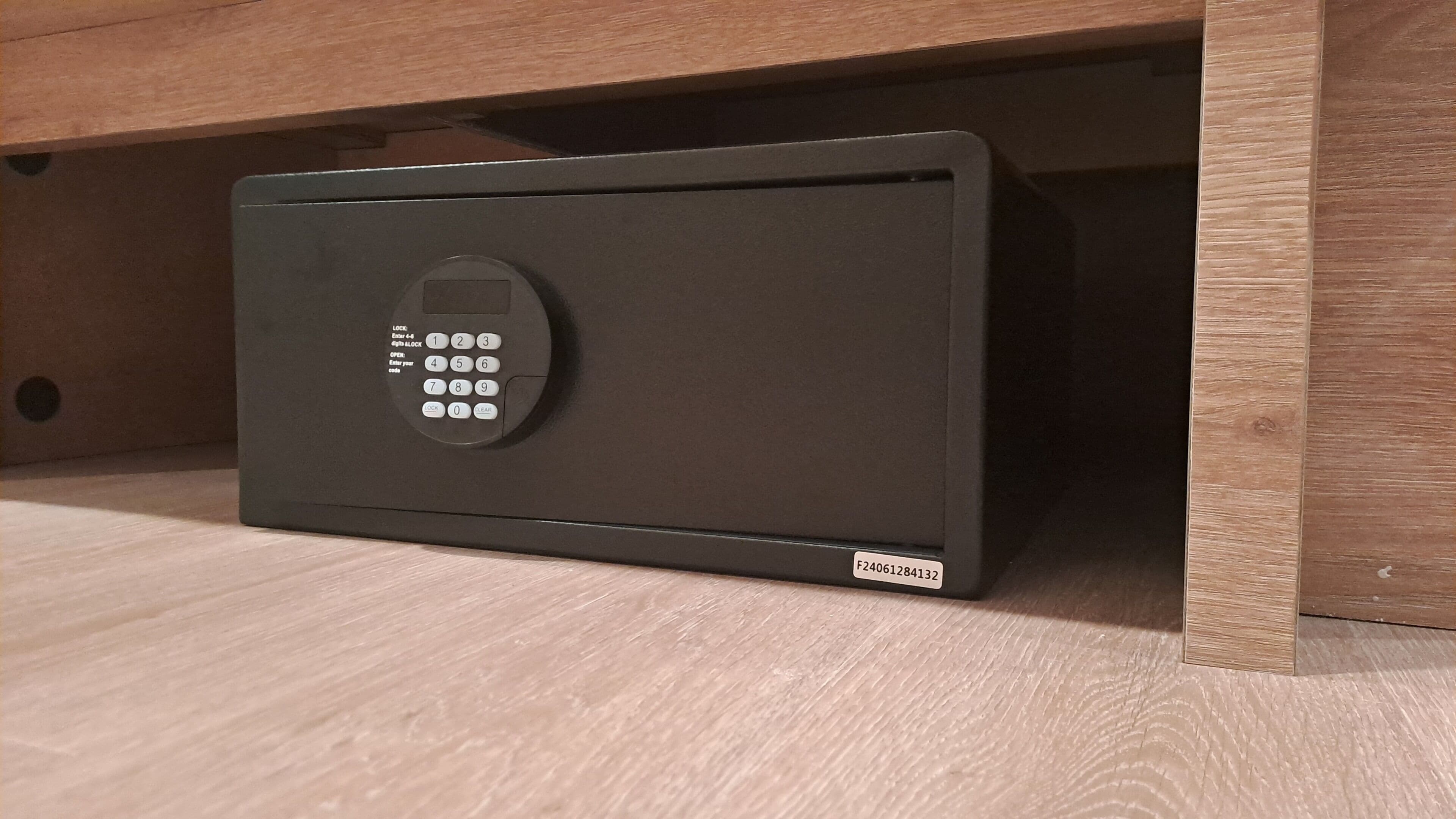 Un coffre-fort noir doté d’un clavier, placé sous une étagère en bois.