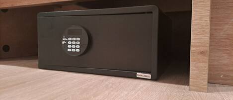 A black safe with a keypad, located under a wooden shelf.