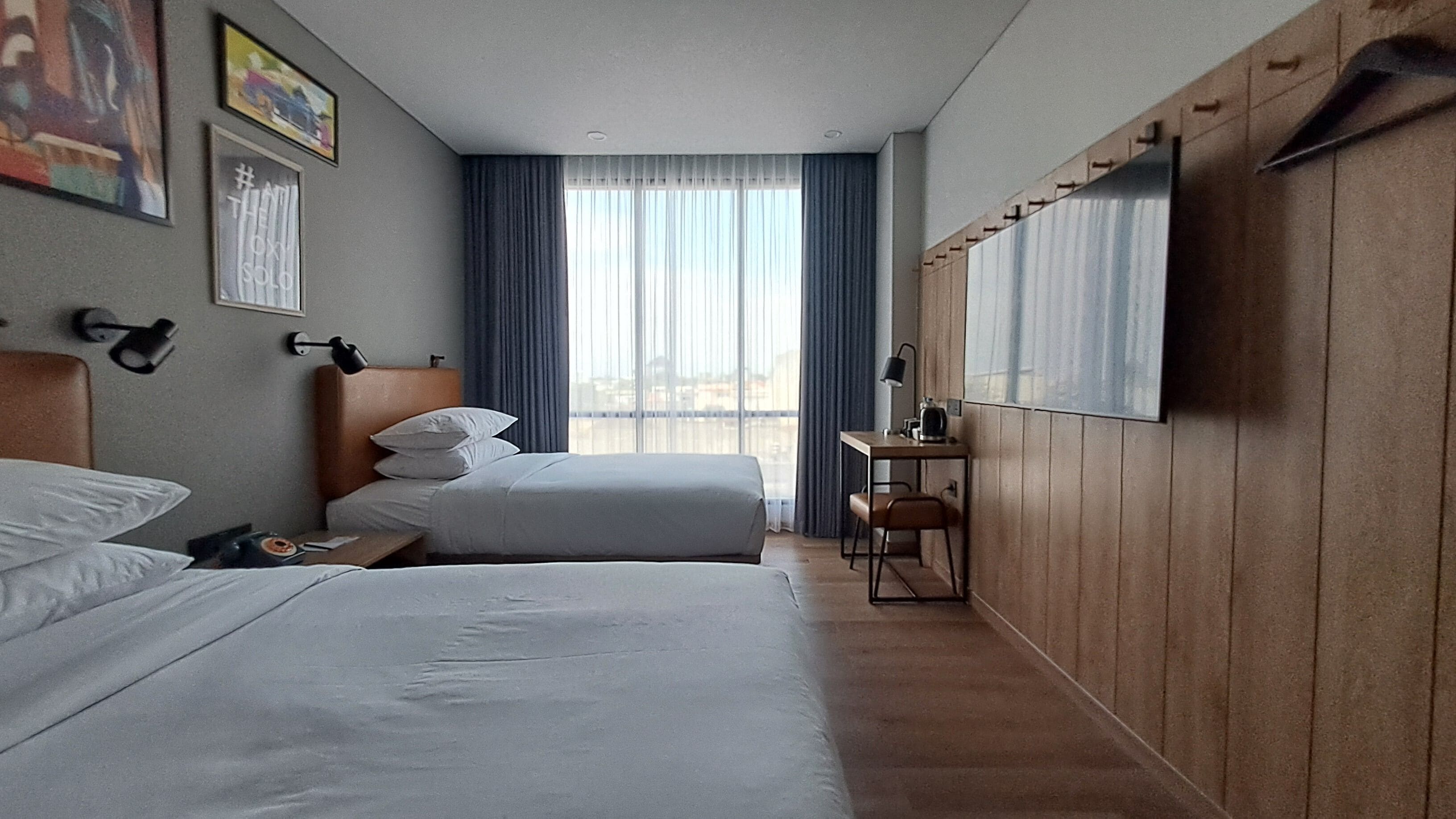 Habitación de hotel con dos camas, un escritorio con silla, televisor en la pared y una ventana con cortinas.