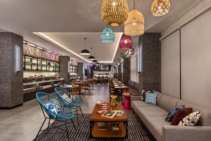 Egy modern szállodai előcsarnok, amelyben egy hosszú recepciós pult, pihenőhelyek és egy bár található.