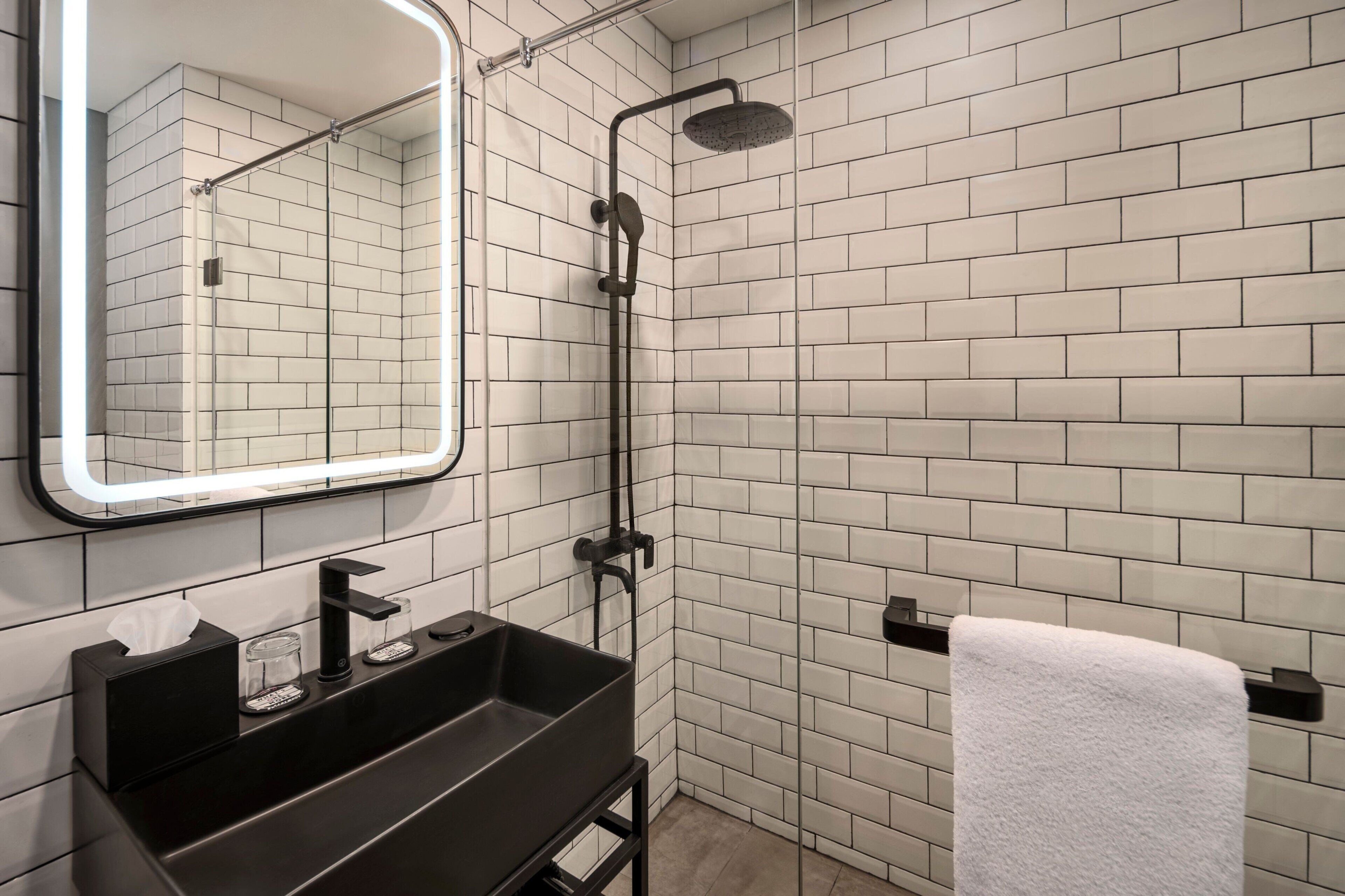 A modern bathroom with a black sink, a mirror with a light, and a shower.