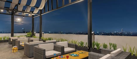 Una terraza en la azotea con mobiliario exterior y vistas a la ciudad al anochecer.