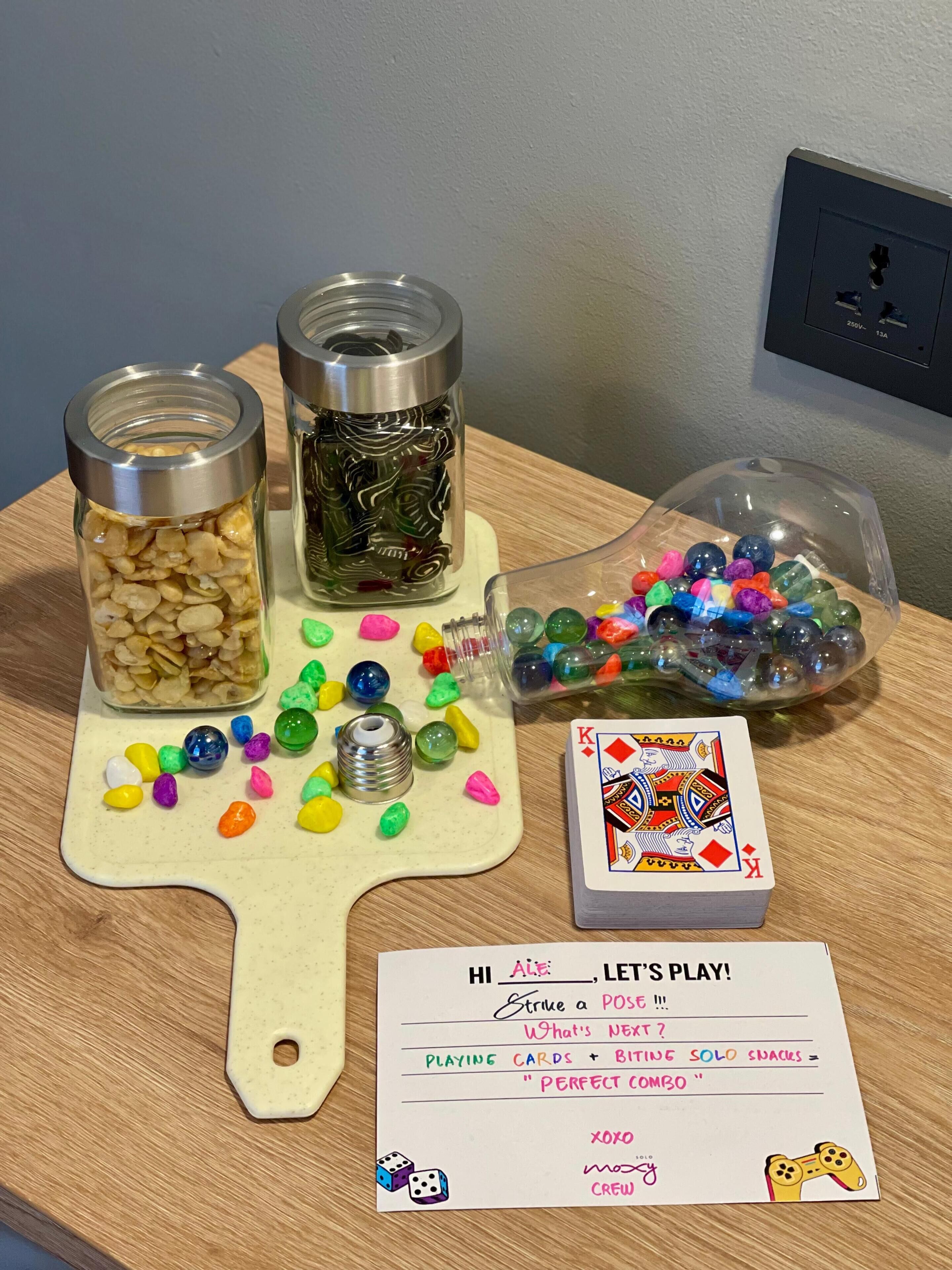 A table with jars of nuts and colorful marbles, a card game, and a sign inviting to play.
