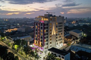 A multi-story hotel with a prominent neon sign, surrounded by a cityscape during twilight. - Moxy Solo (Surakarta)