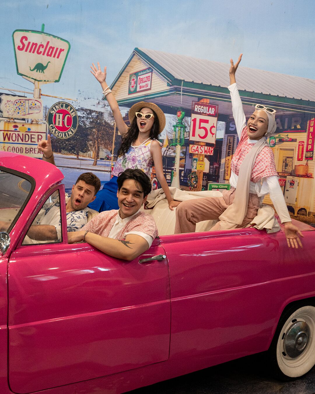 A vintage car with people posing in front of a retro-themed backdrop.