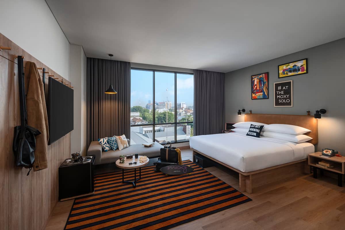 Camera d'albergo moderna con un grande letto, una poltrona, una scrivania e vista sulla città.