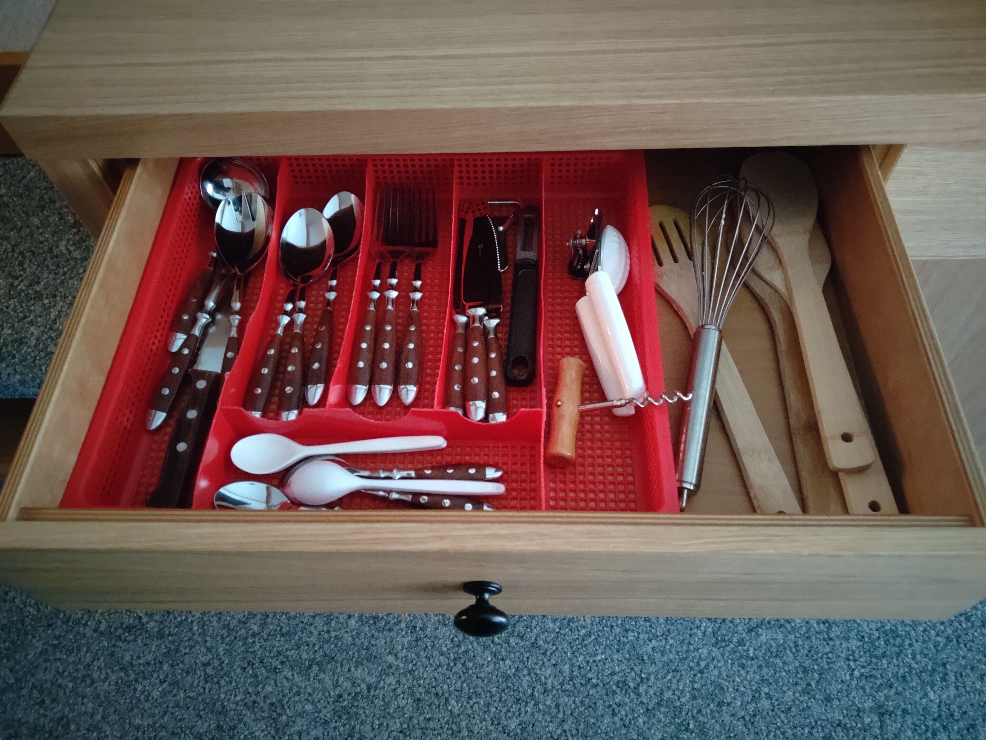 Un cajón con diversos utensilios y herramientas de cocina, incluyendo cuchillos, cucharas y un batidor.