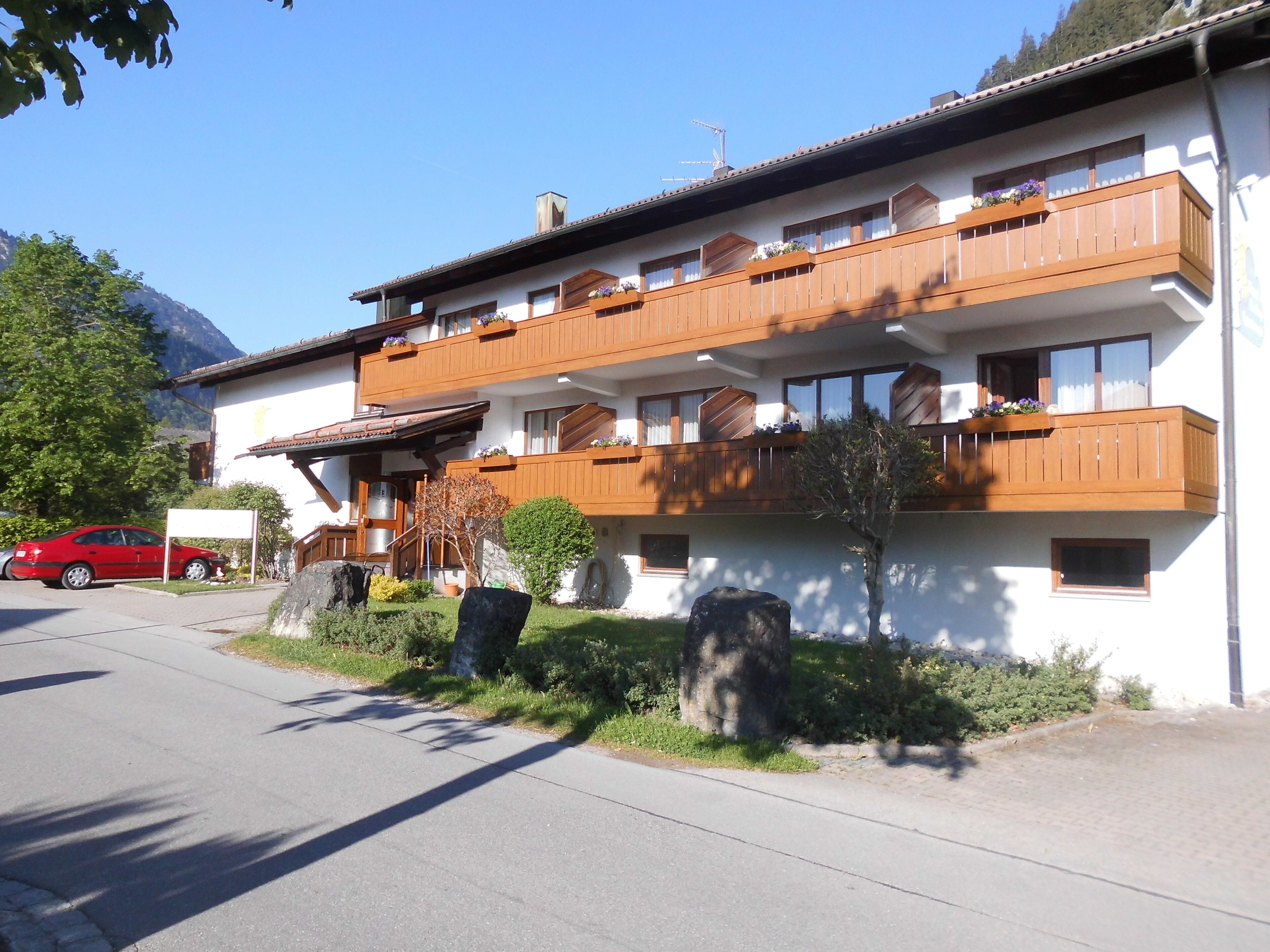 A two-story building with wooden balconies, a red car parked in front, and a mountain in the background.