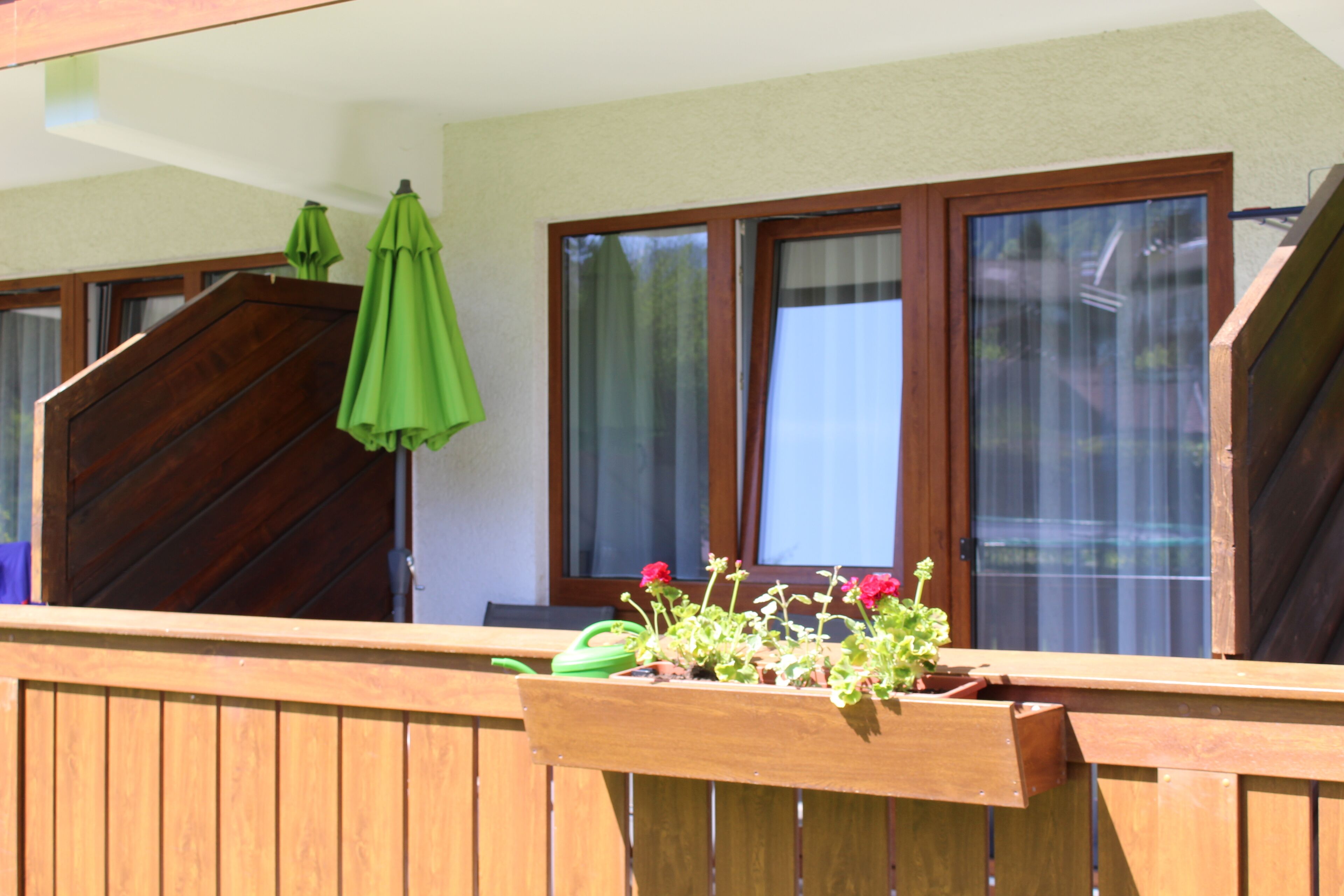 A wooden balcony with a wooden planter box containing flowers and a green umbrella.