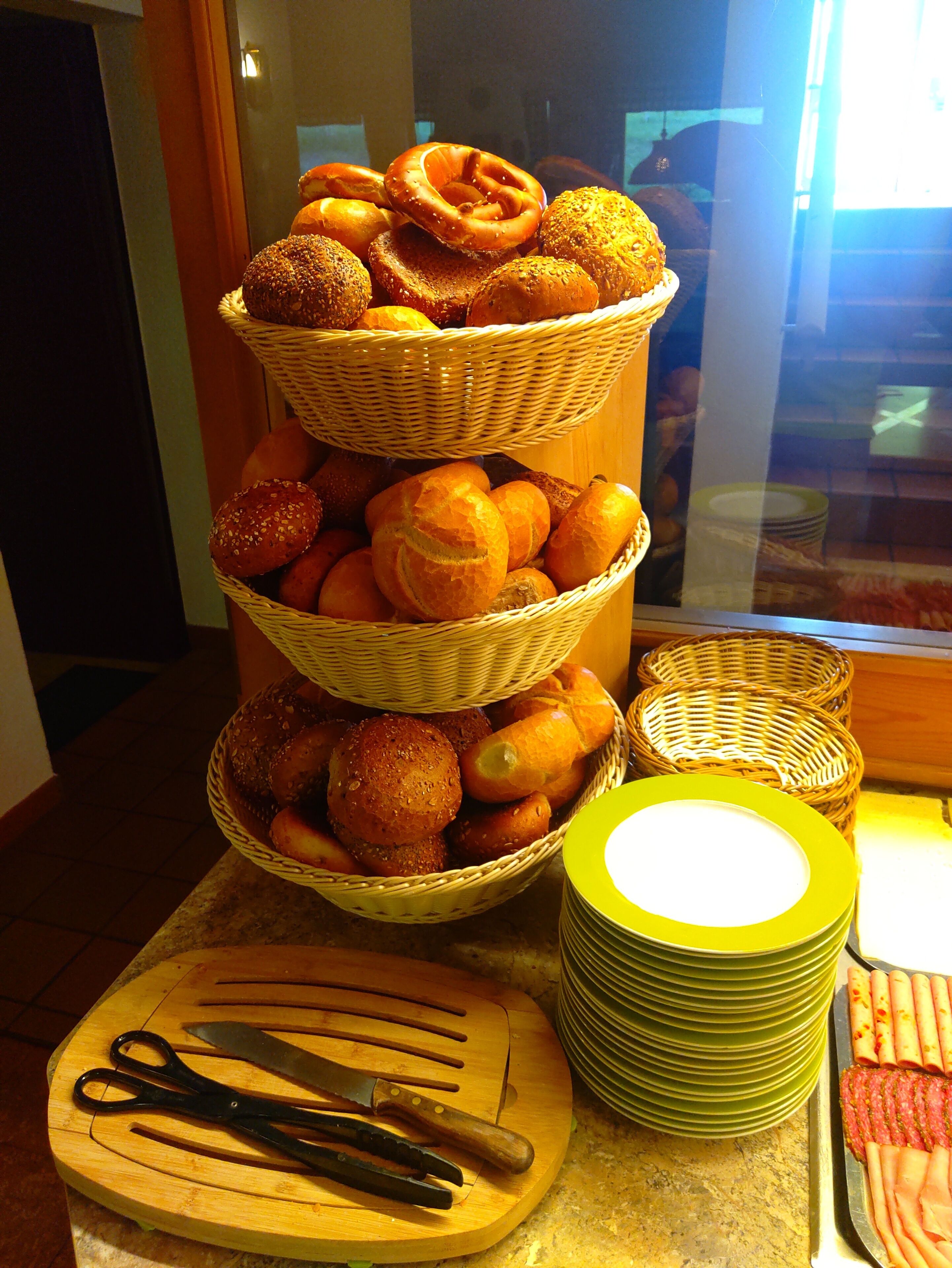 A display of various baked goods in wicker baskets, stacked plates, and kitchen utensils on a countertop.