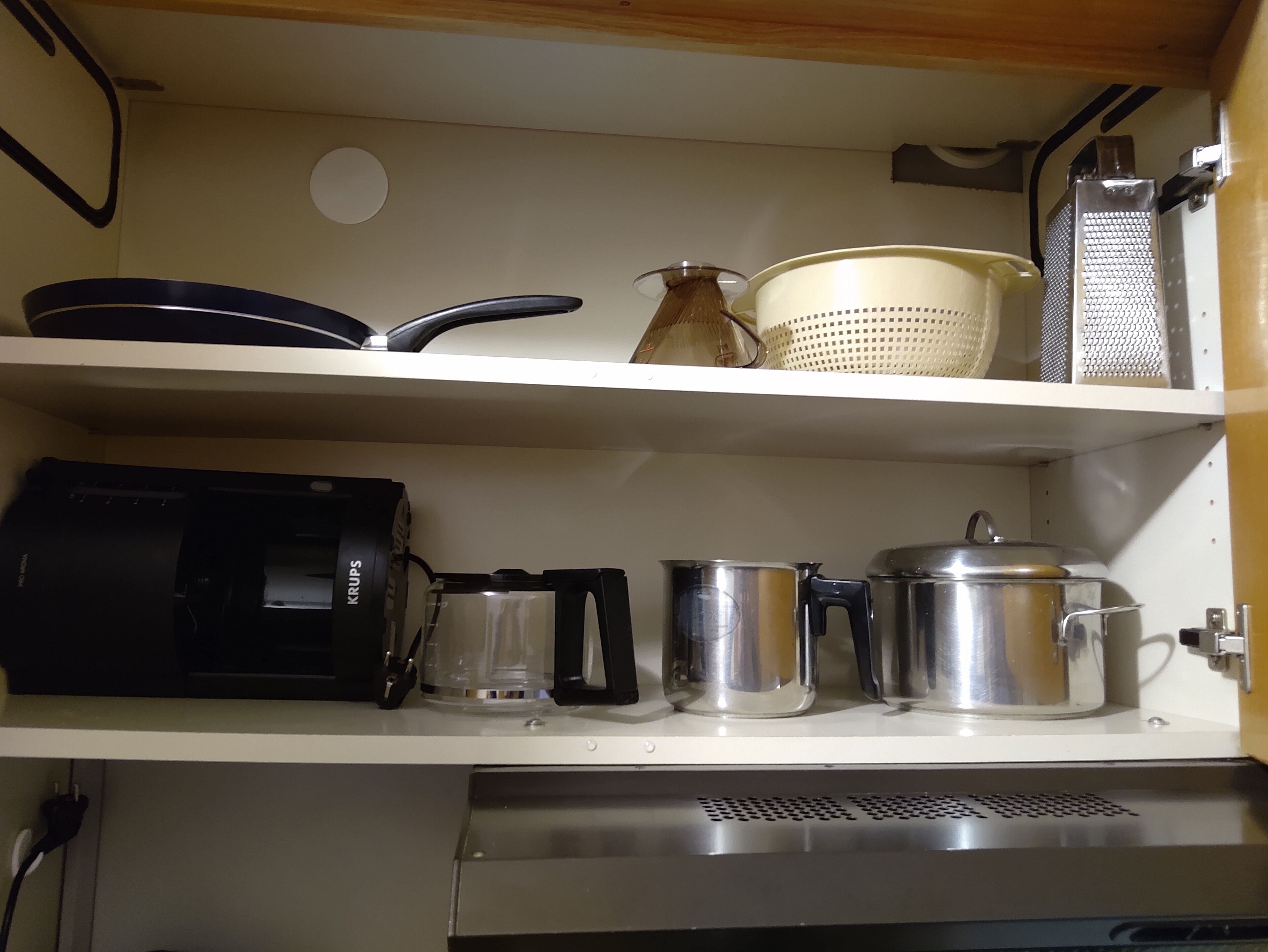 A kitchen with a coffee maker, a kettle, a pot, and a colander on the shelves.