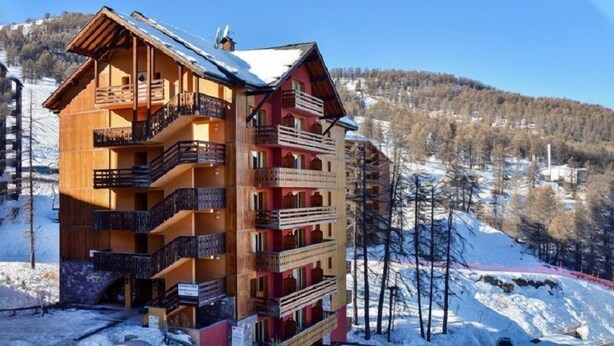 A multi-story wooden building with balconies, set against a snowy mountain backdrop. - Proche des Pistes + Téléski | Duplex avec Balcon (Risoul)