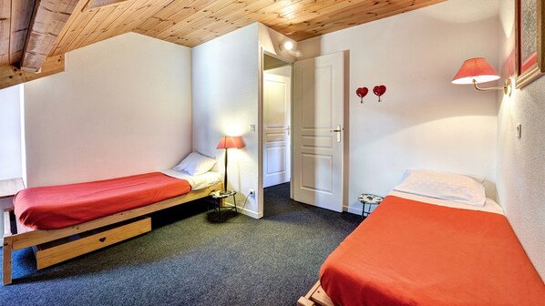 A small, cozy room with two single beds, a nightstand with a lamp, and a door leading to another room.