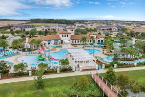 A resort with a large swimming pool, multiple lounge areas, and a view of the surrounding neighborhood.