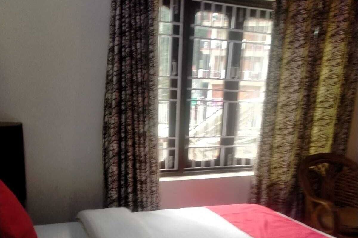 A bed with white and red bedding, a window with metal bars, and a chair.