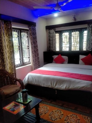 A bedroom with a bed, a table with a book, and a window with curtains. - Moon Peak Cottage (Dharamshala)