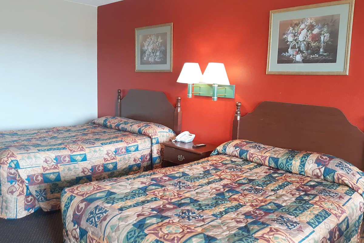 Ein Hotelzimmer mit zwei Betten, einem Nachttisch mit Lampe und zwei gerahmten Bildern an der Wand.