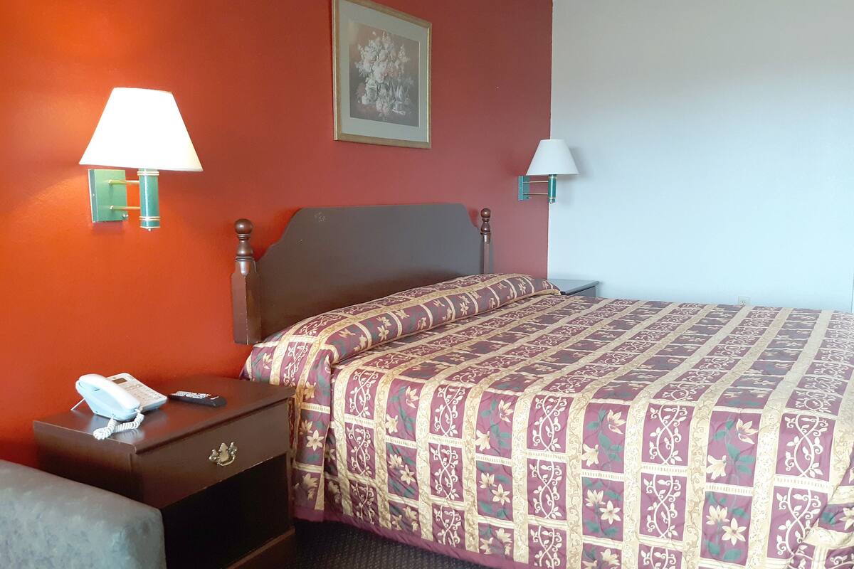 Ein Hotelzimmer mit Bett, Nachttisch mit Lampe, Telefon und einem an der Wand hängenden Bild.