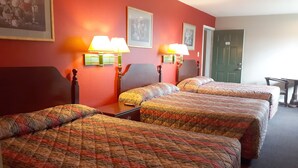Quarto de hotel com três camas, cada uma com colcha estampada, duas luminárias fixadas na parede e quadros enquadrados.
