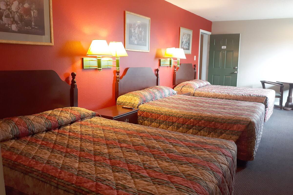 Ein Hotelzimmer mit drei Betten, jedes mit einer gemusterten Tagesdecke, zwei Wandlampen und gerahmten Bildern an der Wand.