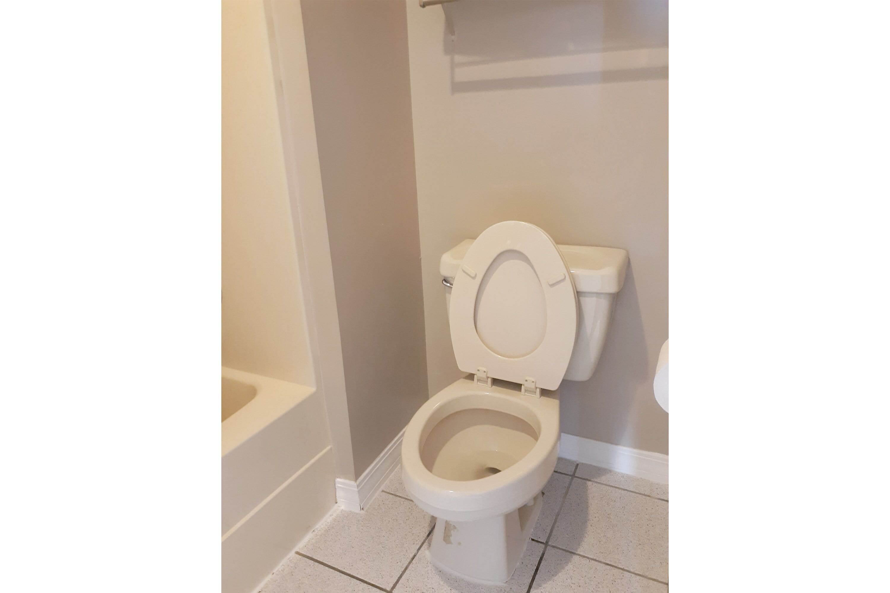 Un inodoro blanco en un baño con paredes color beige y suelo de baldosas blancas.