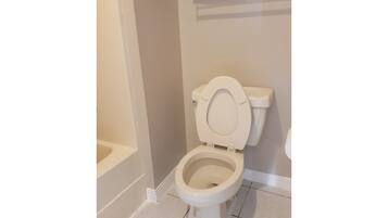 Un inodoro blanco en un baño con paredes color beige y suelo de baldosas blancas.