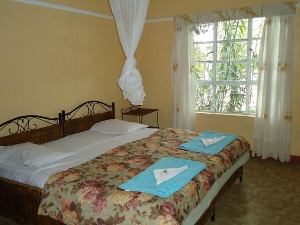 Una habitación con cama, una mesita y una ventana con cortinas.