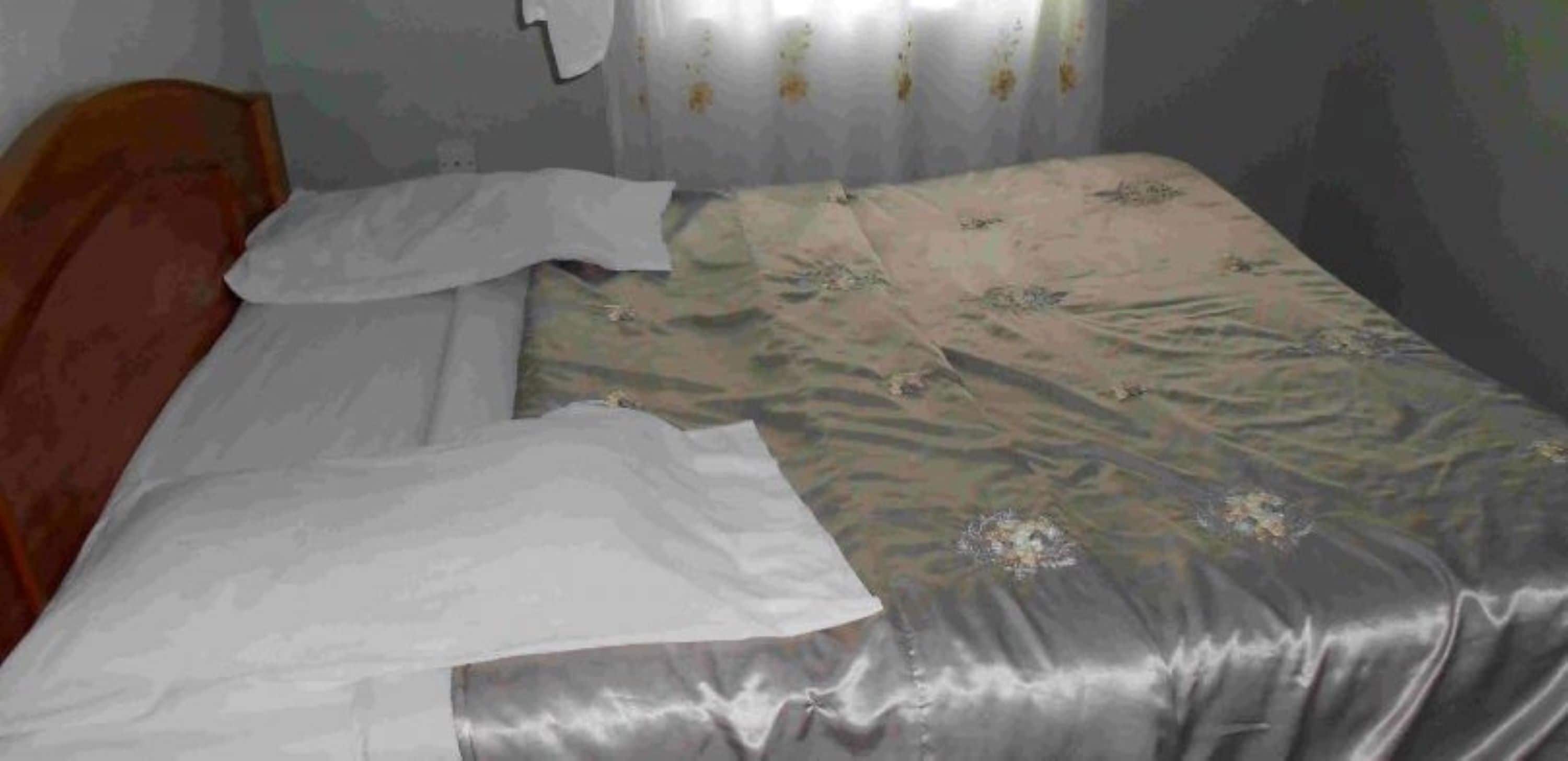 A small, dimly lit room with a single bed, a wooden headboard, and a curtain with floral patterns.