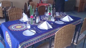 A dining table set with plates, cutlery, glasses, and a bottle of wine, surrounded by wicker chairs.